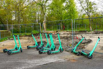 Shared Electric Scooters Parked at a Construction Site with Safety Fence and Tree Background