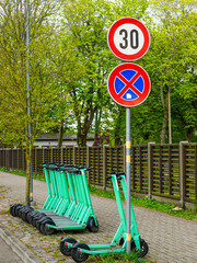 Electric Scooters Parked Near Speed Limit and No Parking Signs on Tree-Lined Urban Sidewalk
