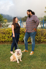 Young couple bonding with their bulldog outdoors. A joyful couple shares a sunny park moment with...