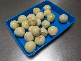 Peeled white onions in a blue plastic tray, ready for cooking.