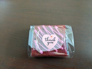 A single brownie, wrapped in clear plastic, with pink icing and a 
