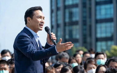 Asian businessman presenting with a microphone at an outdoor corporate conference or public event.