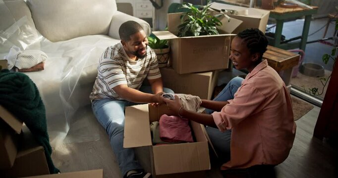 Moving in, couple and unpacking boxes in new house for relocation, property purchase and teamwork. Laugh, black people and help with unboxing clothes in first home with real estate success and above