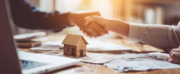 The handshake sealing a home purchase agreement with model house on the table.