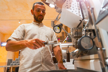 A skilled worker is focused on preparing coffee beans using a roasting machine in a workshop setup...