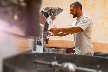A worker carefully operates a coffee roasting machine, preparing arabica and robusta beans in a workshop. The setup is efficient and designed for optimal roasting, showcasing craftsmanship