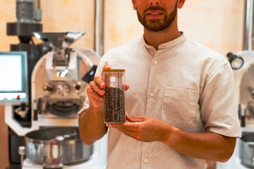 In a roasting workshop, a worker holds a jar filled with roasted arabica and robusta coffee beans,...