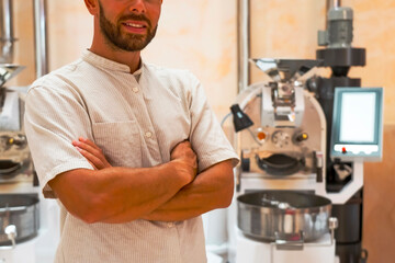 A skilled worker stands confidently in a coffee roasting workshop, preparing arabica and robusta...