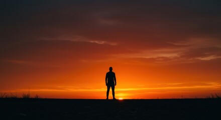 Silhouette of a person standing against a vibrant orange sunset with moody, dramatic sky above.