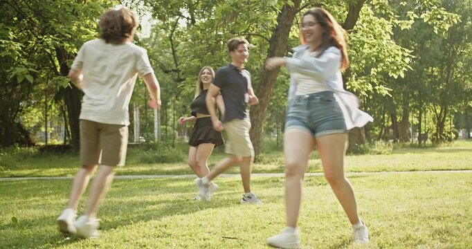 A group of carefree friends playfully chase and run around on the lush green grass of a park during a bright summer day. They are enjoying their youth, freedom, and joyful outdoor activity together.
