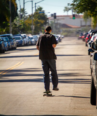 Behind view of a a man skateboarding down a residential street dressed in jeans and a shirt