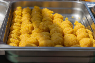 Close-up of yellow savory balls in a serving tray at a food stall