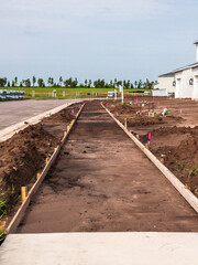 Perspective of future sidewalk, with wooden stakes and formwork in place for pouring of concrete to extend existing sidewalk, alongside a new street in a suburban residential development in Florida