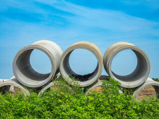 Three new stormwater pipes of precast concrete on top of a row of others at the weedy edge of a large suburban construction site in southwest Florida. Motifs of interconnection and the environment.