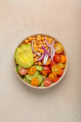 Healthy chickpea salad with ripe avocado, juicy cherry tomatoes, crisp cucumber, and red onion slices. Perfect for a nutritious and healthy meal, light beige background