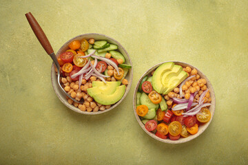 Two bowls of healthy chickpea salad with ripe avocado, juicy cherry tomatoes, crisp cucumber, and red onion slices. Perfect for a nutritious and healthy meal, light green background