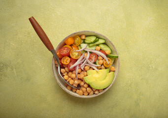 Healthy chickpea salad with ripe avocado, juicy cherry tomatoes, crisp cucumber, and red onion slices. Perfect for a nutritious and healthy meal on light green background