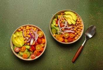 Two bowls of healthy chickpea salad with ripe avocado, juicy cherry tomatoes, crisp cucumber, and red onion slices. Perfect for a nutritious and healthy meal on green background