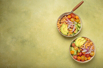 Two bowls of healthy chickpea salad with ripe avocado, juicy cherry tomatoes, crisp cucumber, and red onion slices. Perfect for a nutritious and healthy meal, light green background, copy space