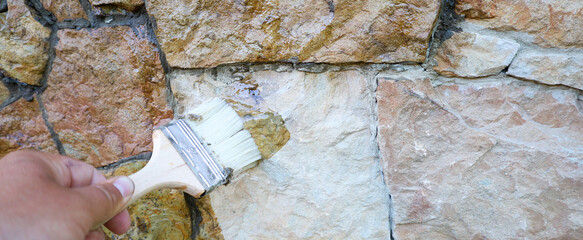 Facade renovation: a craftsman's hand applies a special solution to a stone wall, giving it a fresh...
