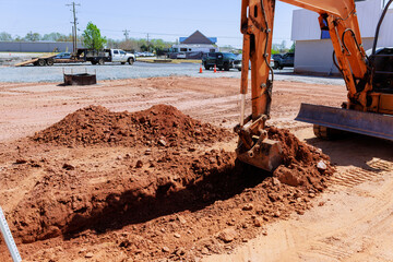 Excavator works on construction site creating trench while trucks are parked nearby during works...