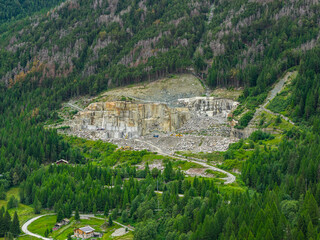 Aerial view of a marble quarry in the Italian Alps, carved into the forested mountain slope with...