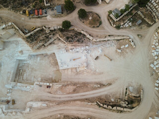 Top‑down view of industrial operations in a quarry with machinery and large light‑stone cuts