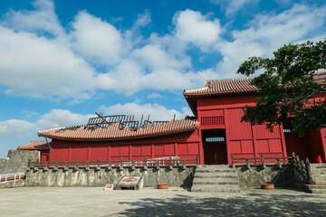 The surviving red Nanden hall stands beside the burnt, skeletal ruins of Shuri Castle's main...