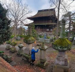 A curious visitor in a blue coat touches an ancient, mossy stone lantern in the serene garden of...
