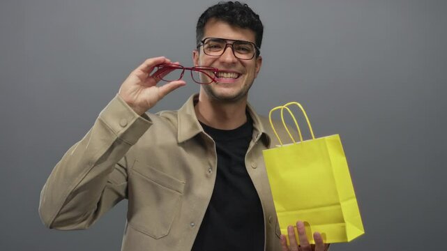 Man wearing glasses is pulling a paper bag in a studio with hispanic young colored background and showing male specs clearly.