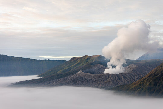 View of Mount Bromo's volcanic peak piercing through a sea of ethereal fog, contrasting with the rugged terrain, Mount Bromo Volcano, East Java, Indonesia.