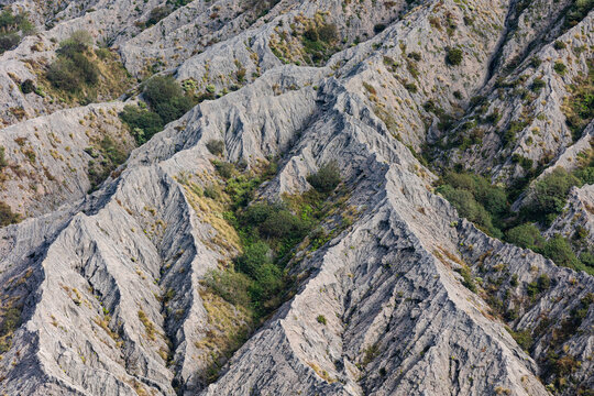 View of rugged, arid terrain etched with deep ravines and sparse vegetation creates a textured landscape, Mount Bromo, East Java, Indonesia.