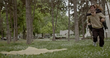 Friends having fun in a park. A young man gives his female friend a piggyback ride. They're both laughing and enjoying their time together.