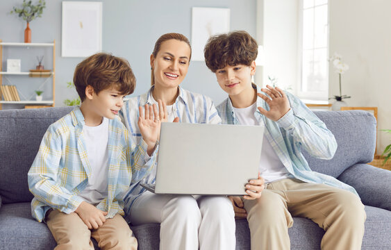 Happy mother is with two sons, having an online video call on a laptop at home in the living room. Moment of positive family communication and leisure time spent together in the internet.