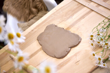 Clay workshop setup with rolled-out clay, rolling pin, tools, and fresh chamomile flowers on a wooden table. Cozy atmosphere and natural materials in a creative studio setting