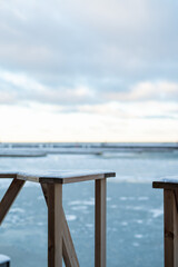 Serene winter photo, taken in Tallinn, Estonia, captures a view over an icy body of Baltic Sea in Haven Kakumäe harbor. In the foreground simple wooden railing with light snow dusting. 