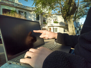 College student using laptop outdoors is pointing at the screen