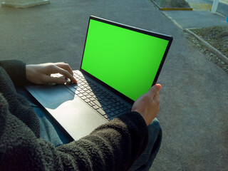 Student working on laptop with green screen outdoors on campus