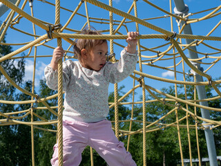 Young girl climbing and playing on yellow rope structure in modern outdoor playground on a sunny...