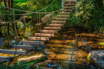 Small hanging bridge in a garden or park  over small river or pond