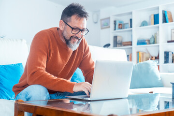 Mature man using laptop at home with mixed expressions. Remote work, digital lifestyle, emotional...