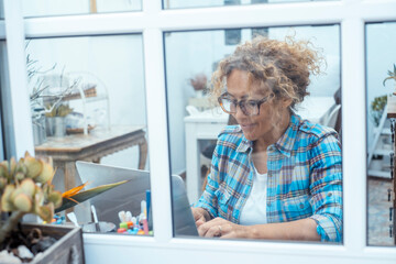 Curly-haired woman in her 40s using a laptop at home with varied expressions. Remote work, digital...