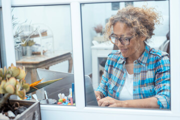 Curly-haired woman in her 40s using a laptop at home with varied expressions. Remote work, digital...