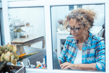 Curly-haired woman in her 40s using a laptop at home with varied expressions. Remote work, digital...