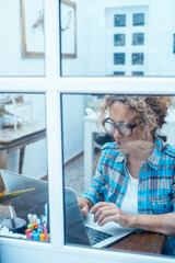 Curly-haired woman in her 40s using a laptop at home with varied expressions. Remote work, digital...