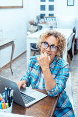 Curly-haired woman in her 40s using a laptop at home with varied expressions. Remote work, digital...