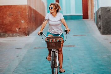 Smiling curly-haired woman in her 40s riding a city bicycle outdoors. Healthy lifestyle,...