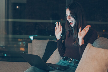 Smiling young woman using laptop at night at home. Online dating, chatting with friends, social video calls, modern technology, digital lifestyle and the joy of connecting with new people