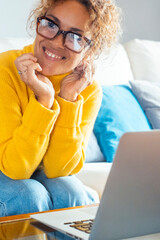 Attractive woman sitting on white sofa at home smiles, looks at her laptop computer  screen and...
