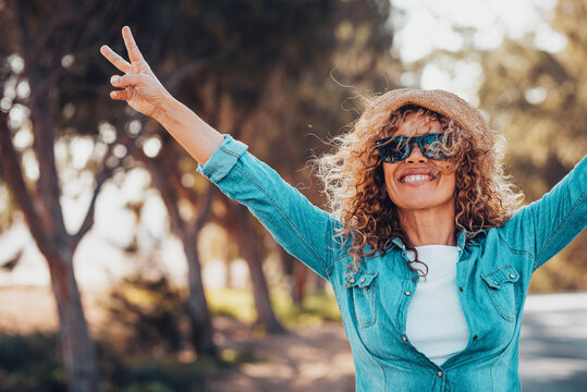 Portrait of wonderful white female model with curly blonde hair expressing energy on a good day in Europe. Beautiful curly woman smiling and walking with trees behind her.